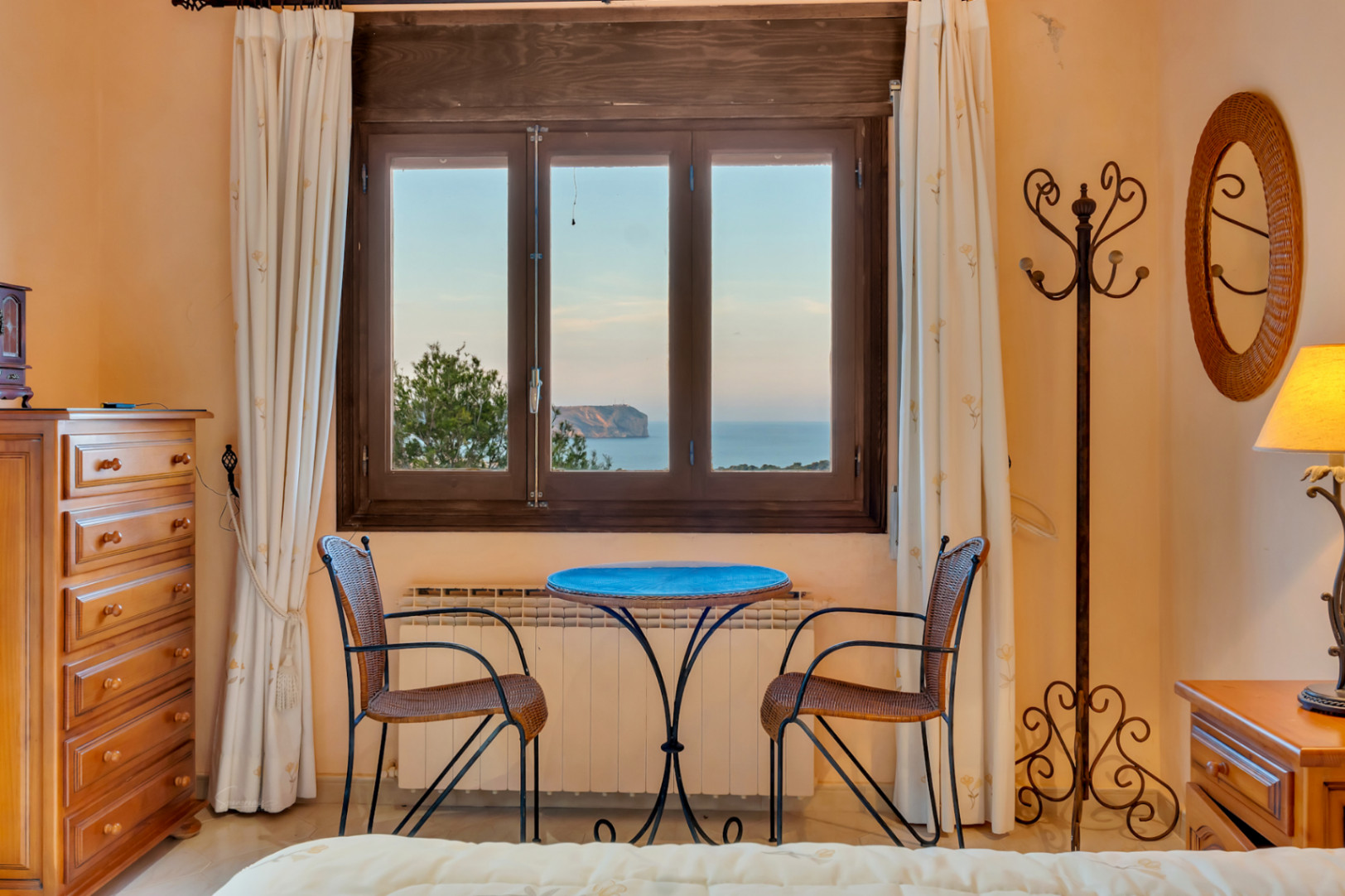 Sitzbereich im Schlafzimmer mit Korbstühlen und Holzkommode, mit direktem Blick auf das Mittelmeer und das Cabo San Antonio.