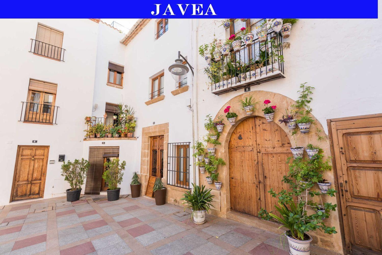 Traditionelle Fassade in der Altstadt von Jávea mit Holztüren, Rundbögen aus Tosca-Stein und dekorativen Keramik-Blumentöpfen an weißen Wänden.