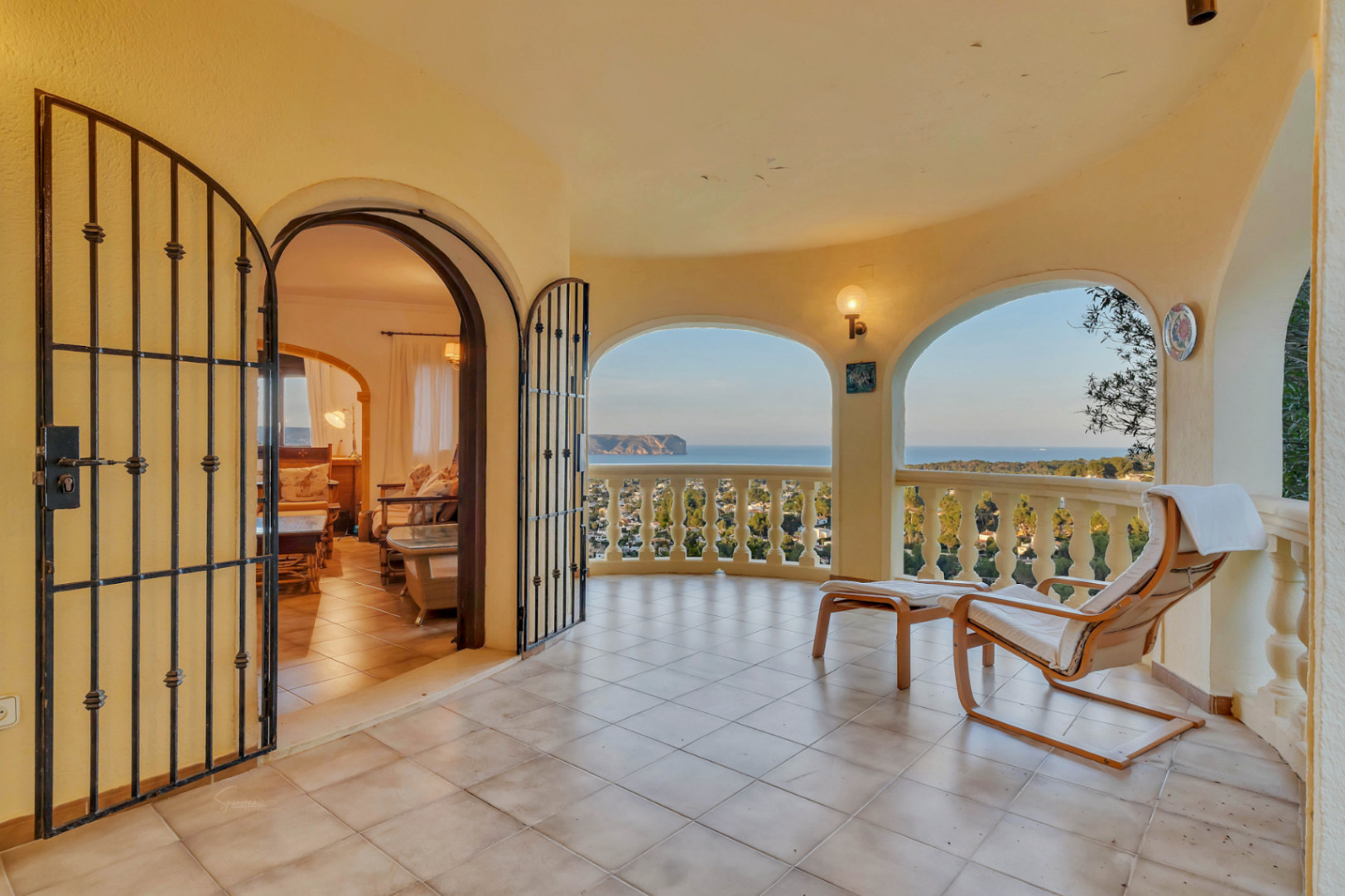 Überdachte Terrasse mit Rundbögen und klassischer Balustrade mit Blick auf das Cabo San Antonio. Gefliester Boden und Zugang zum Wohnzimmer durch ein schmiedeeisernes Tor.