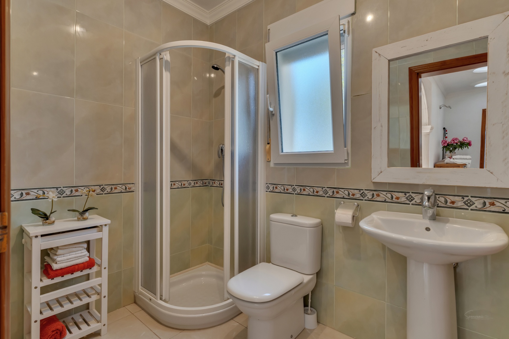 Badezimmer mit einer abgerundeten Eckdusche, einem Standwaschbecken und hell gefliesten Wänden mit dekorativer Bordüre.