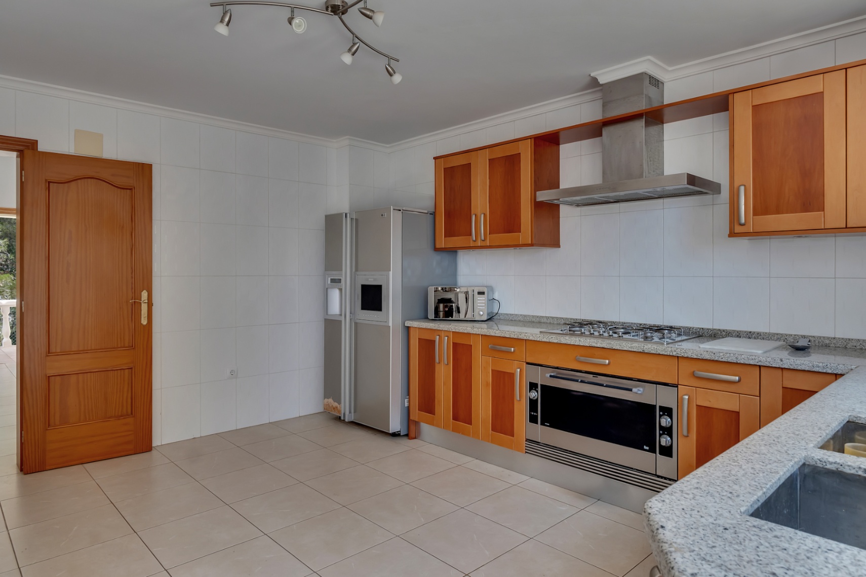 Einbauküche mit Holzschränken, Arbeitsplatten aus grauem Granit und Edelstahlgeräten, darunter ein amerikanischer Kühlschrank und ein extrabreiter Backofen.