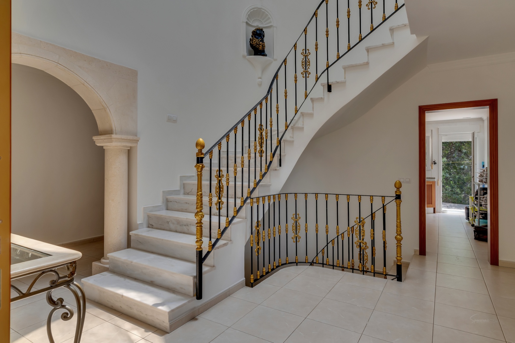 Eingangshalle mit Marmortreppe, kunstvollem schmiedeeisernem Geländer mit Goldverzierungen und einem Steinbogen mit klassischer Säule.