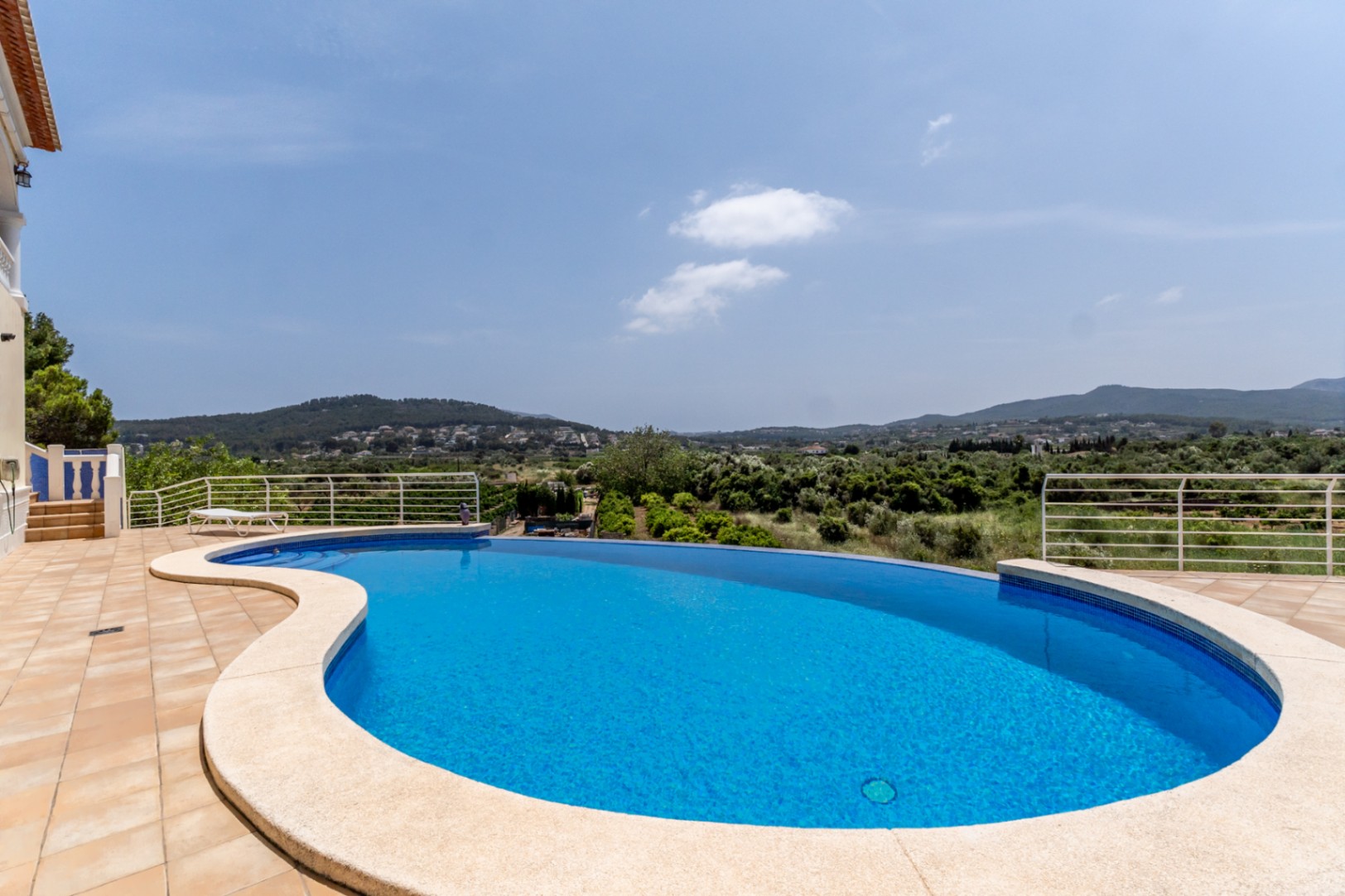 Geschwungener Infinity-Pool auf einer gefliesten Terrasse mit weitem Panoramablick über das grüne Tal und die umliegende Berglandschaft von Jávea.