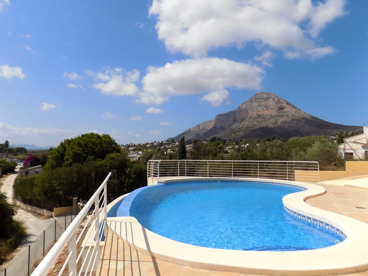 Geschwungener Infinity-Pool mit Panoramablick auf das Montgó-Massiv, umgeben von einer gefliesten Terrasse und weißen Sicherheitsgeländern.