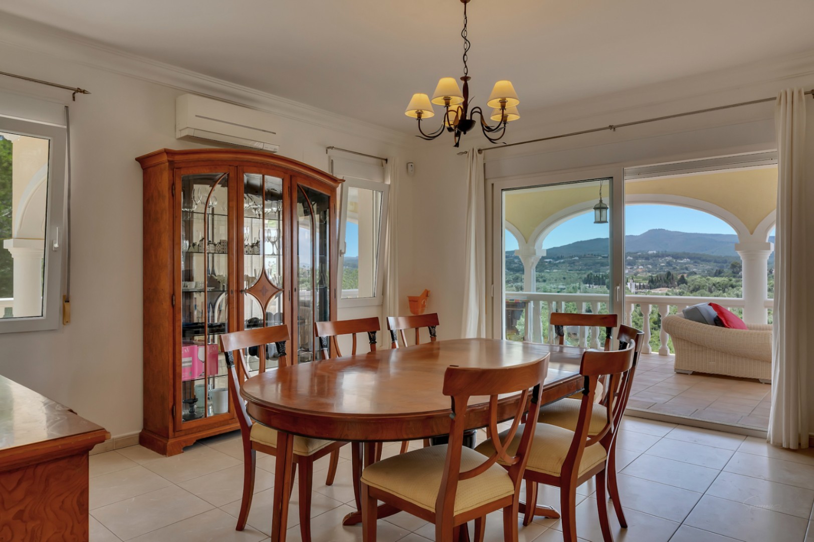 Großzügiges Esszimmer mit ovalem Holztisch, klassischer Vitrine und direktem Zugang zur Terrasse mit Panoramablick auf das Tal und den Montgó.