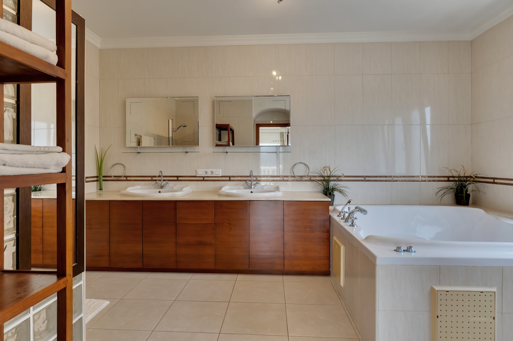 Hauptbadezimmer mit Doppelwaschtisch aus Holz, zwei Spiegeln und einer großen, in helle Fliesen eingefassten Hydromassage-Badewanne.