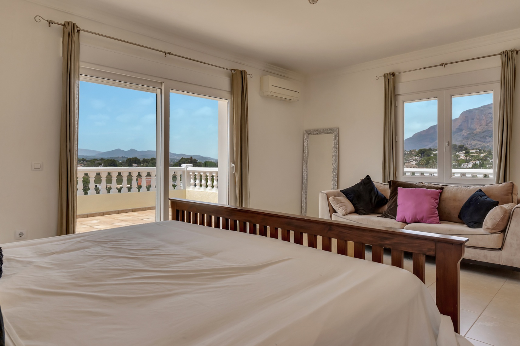 Hauptschlafzimmer mit dunklem Holzbettenrahmen, Sitzecke und Zugang zur Terrasse mit weitem Blick auf das Montgó-Massiv.