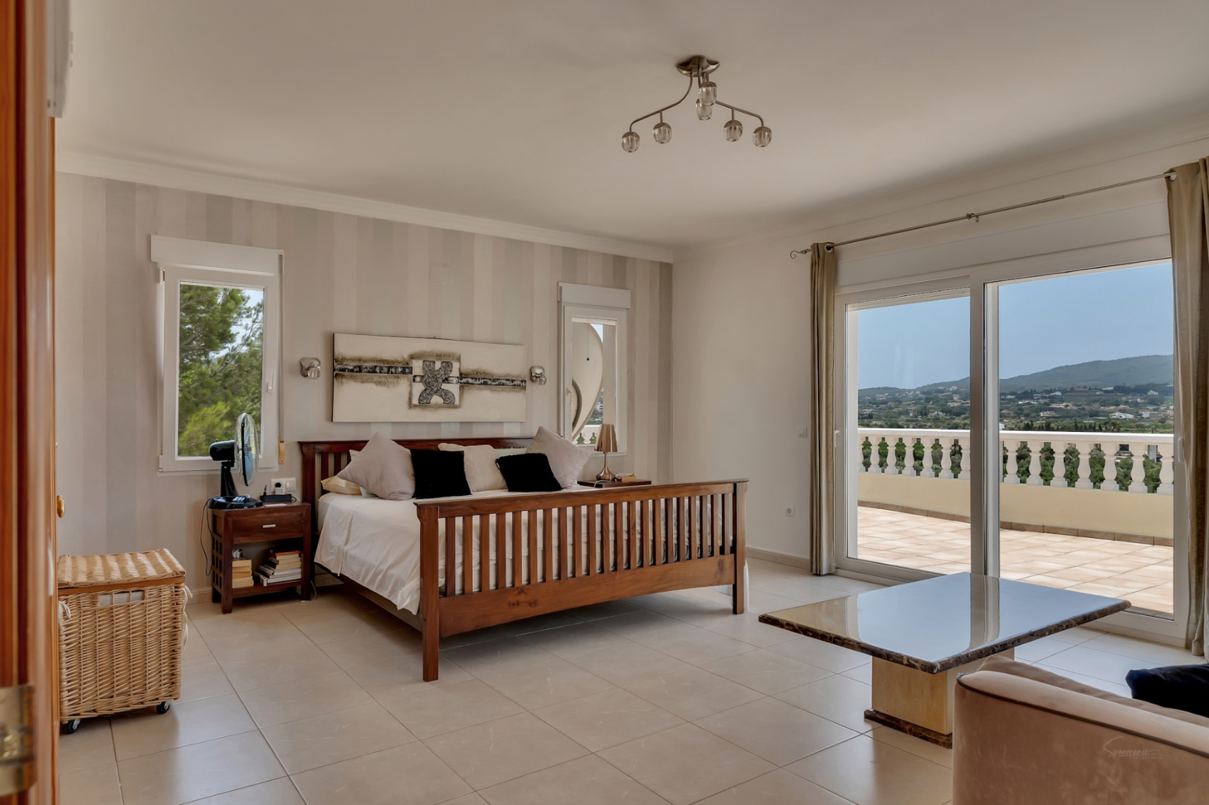 Hauptschlafzimmer mit Holzbettenrahmen, gestreifter Akzentwand und großen Glasschiebetüren, die auf eine Terrasse mit Panoramablick über das Tal führen.