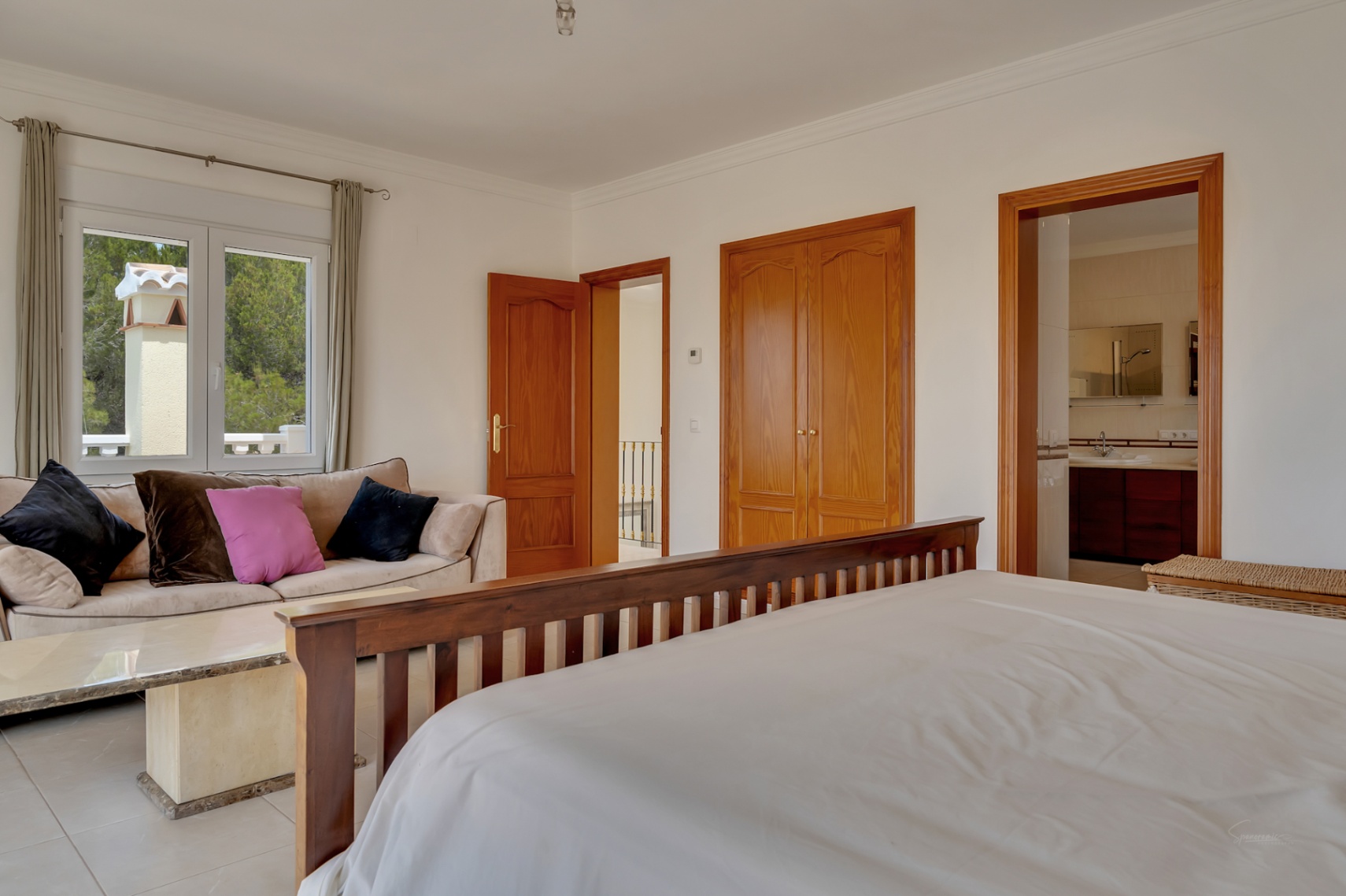 Hauptschlafzimmer mit integrierter Sitzecke, Einbauschränken aus Holz und En-Suite-Badezimmer. Große Fenster bieten Blick auf die bewaldete Umgebung.