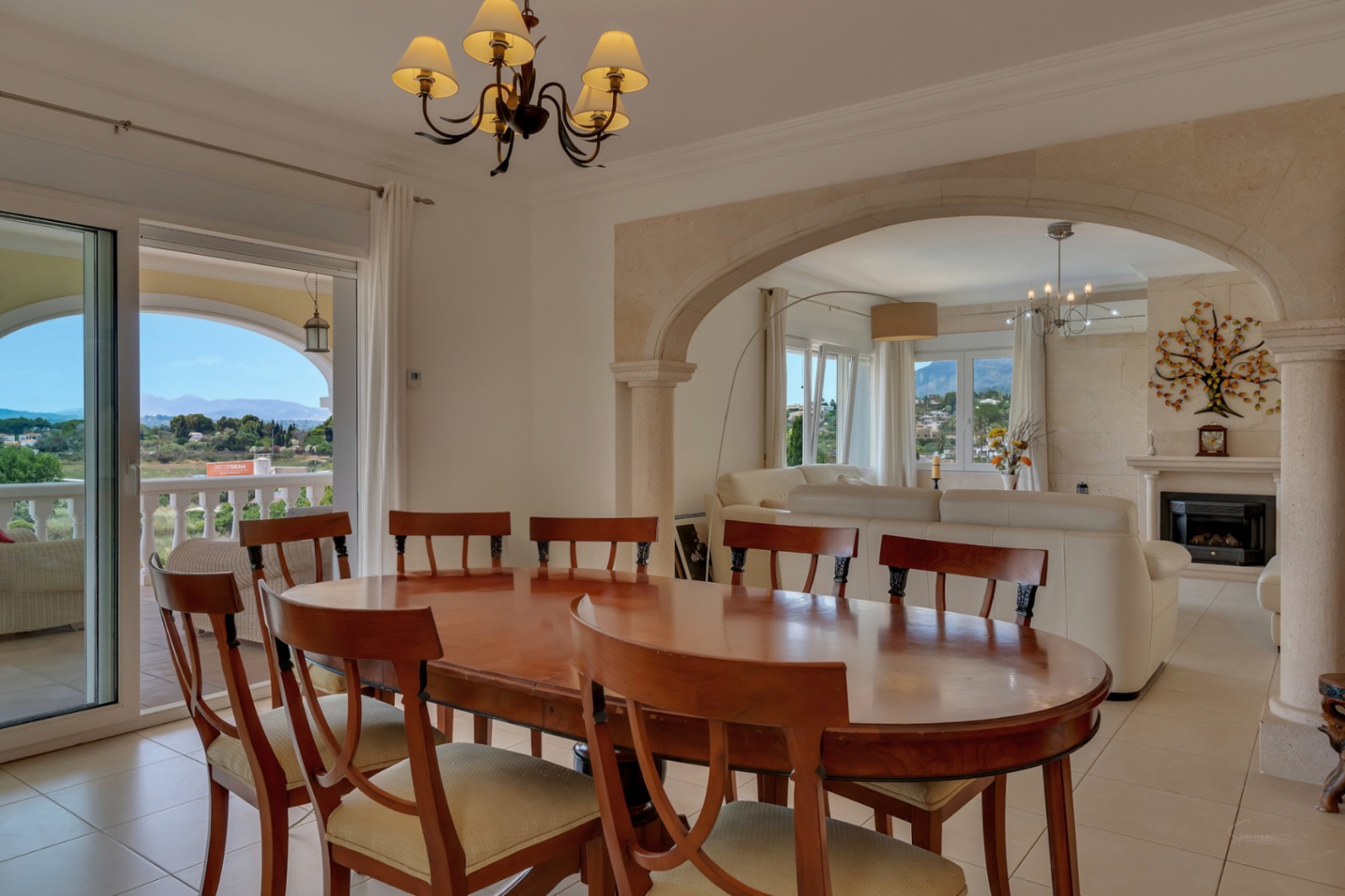 Heller Essbereich mit Holztisch, verbunden mit dem Wohnzimmer durch einen Tosca-Steinbogen, mit direktem Zugang zur Terrasse und Panoramablick ins Tal.
