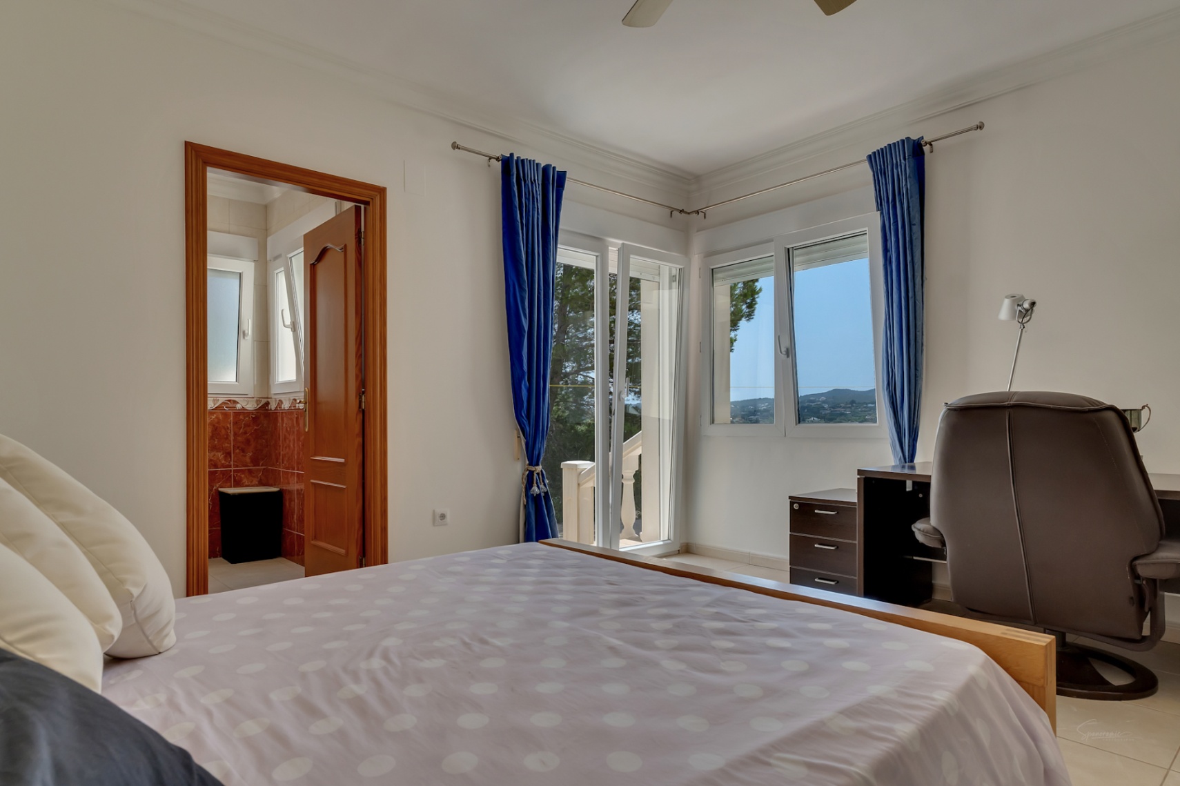 Helles Schlafzimmer mit direktem Terrassenzugang, integriertem Arbeitsbereich und En-Suite-Badezimmer mit rötlichen Marmorfliesen.