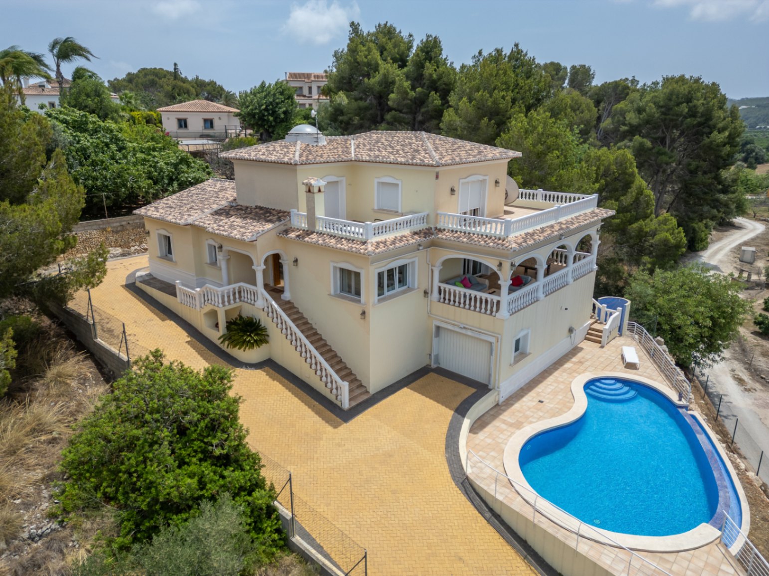 Luftaufnahme der mediterranen Villa mit nierenförmigem Pool, weitläufigen Terrassen mit weißen Balustraden, einer Rundbogennaya und markanter Glaskuppel auf dem Dach.