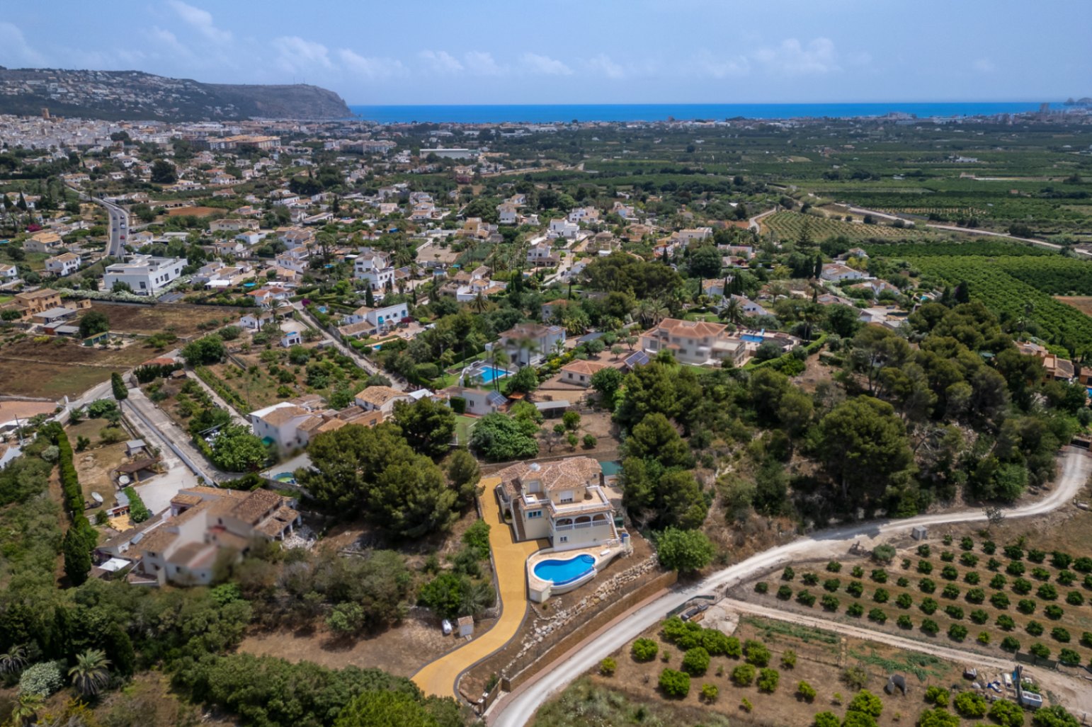 Luftaufnahme der Villa in Hanglage mit geschwungenem Infinity-Pool, eingebettet in eine mediterrane Landschaft mit weitem Blick auf das Meer und das Tal.