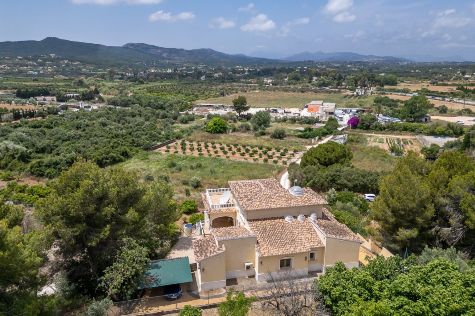 Luftaufnahme der Villa mit Terrakotta-Ziegeldächern, zentraler Glaskuppel und Oberlichtern, eingebettet in die mediterrane Landschaft mit Blick auf die Berge.
