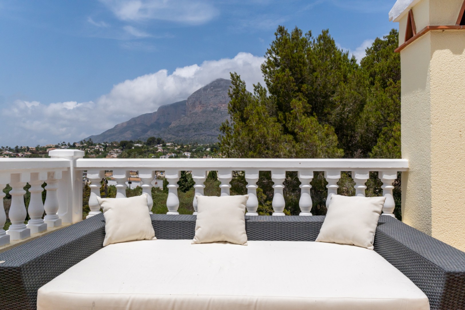 Obere Terrasse mit großem Rattan-Daybed und klassischer weißer Balustrade, mit direktem Panoramablick auf den Berg Montgó und das Tal.