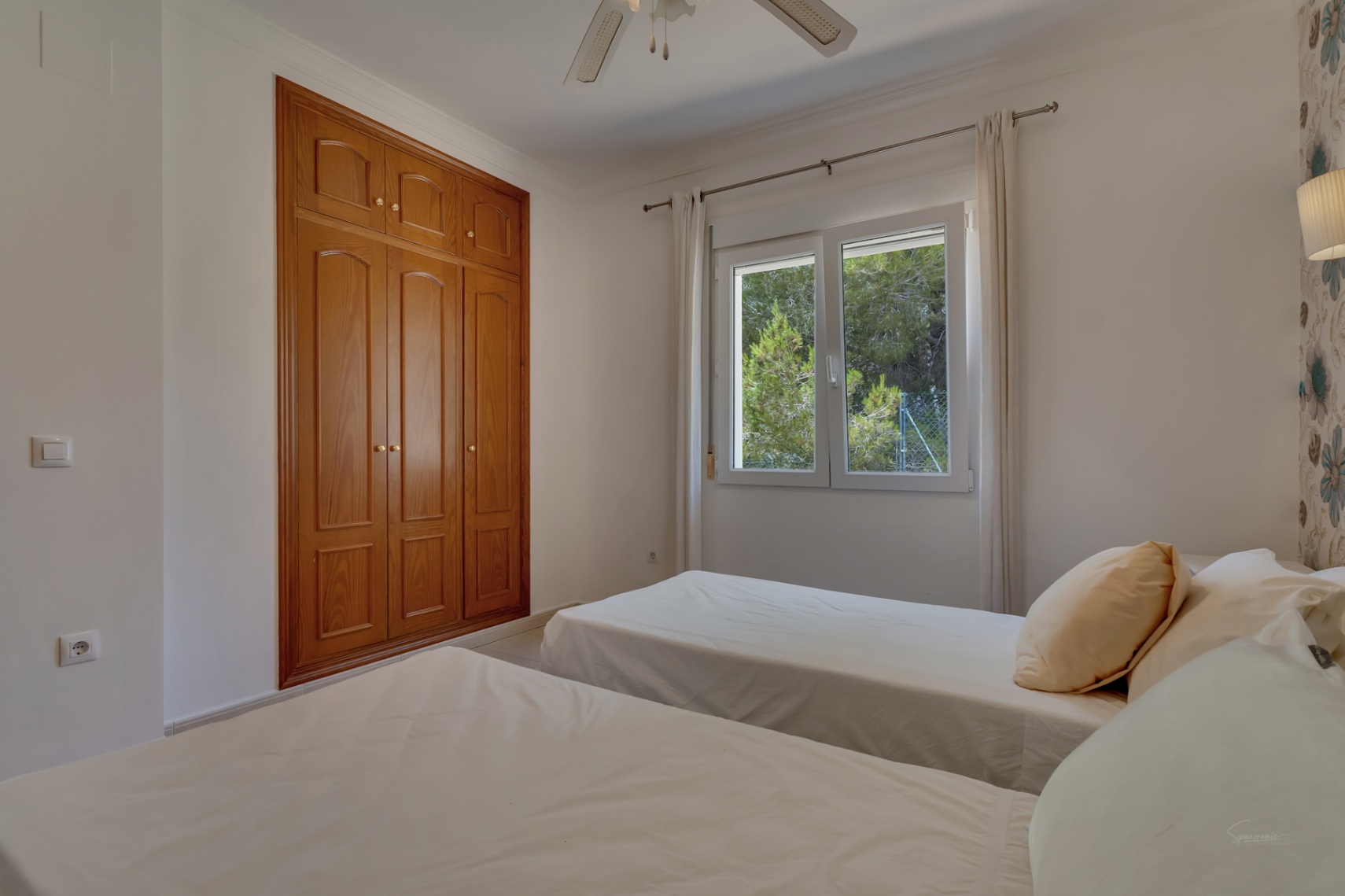 Schlafzimmer mit zwei Einzelbetten, Einbauschränken aus Holz, Deckenventilator und Fenster mit Blick auf die umliegende Natur.