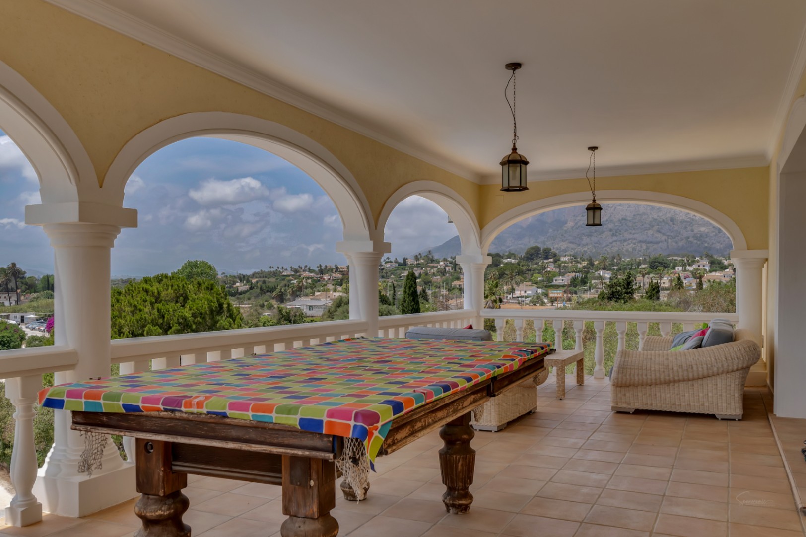 Überdachte Terrasse mit klassischen Rundbögen, Billardtisch und Loungebereich, die einen Panoramablick auf den Montgó und das Tal von Jávea bietet.