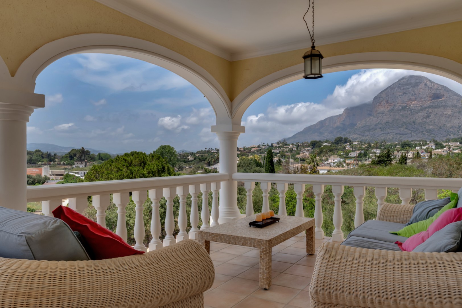 Überdachte Terrasse mit Rundbögen, Korbmöbeln und Panoramablick auf das Montgó-Massiv und die umliegende Landschaft von Jávea.