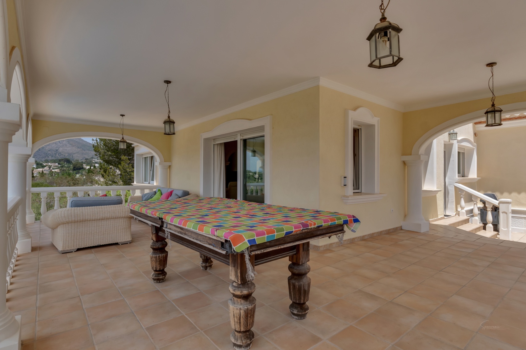Überdachte Terrasse mit traditionellen Rundbögen, Terrakottaboden und einem Billardtisch. Sie bietet einen Panoramablick auf das Tal und den Berg Montgó.