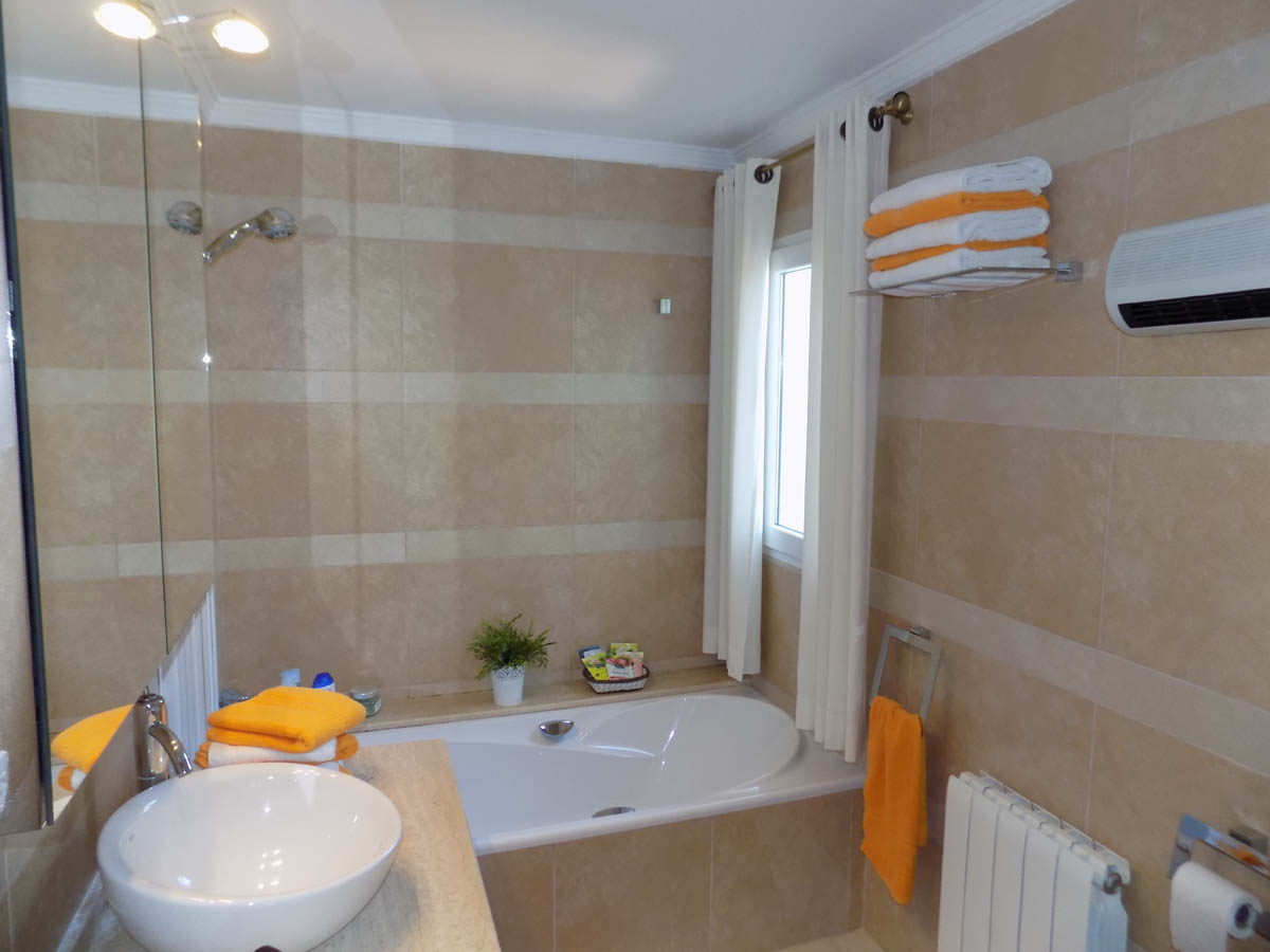 Badezimmer mit Einbauwanne, Aufsatzwaschbecken auf einer Steinarbeitsplatte und cremefarbenen Wandfliesen mit horizontalen Streifen.