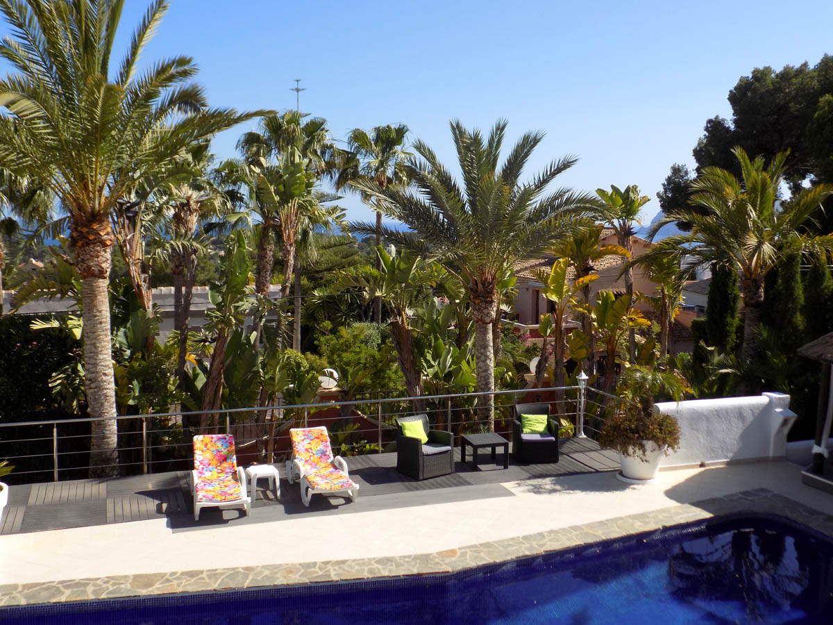 Erhöhte Terrasse mit Pool, Sonnendeck aus dunklem Holz und Meerblick, umgeben von prächtigen Palmen und mediterraner Bepflanzung.