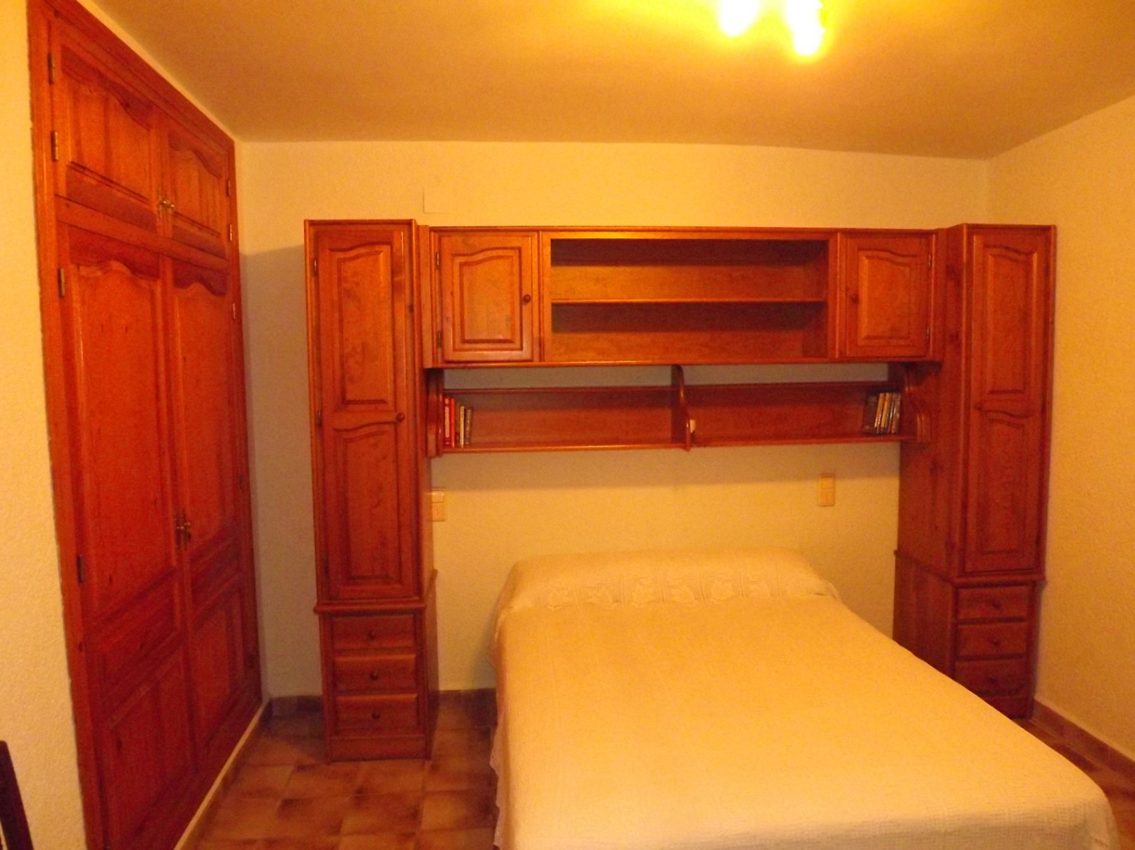 Schlafzimmer mit Massivholzmöbeln, bestehend aus einem Einbauschrank und einer Überbaubrücke mit Regalen und Schubladen über dem Bett.