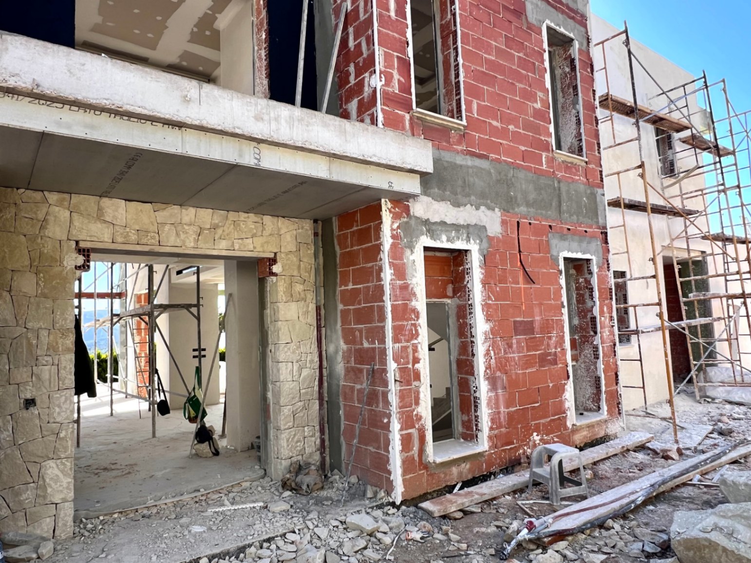 Aktueller Baufortschritt mit Ziegelmauerwerk, Natursteinverkleidung und großzügigen Fensteröffnungen für eine moderne, helle Architektur.