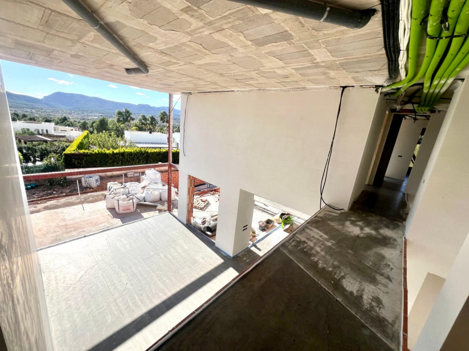 Baufortschritt mit doppelt hoher Deckenstruktur, sichtbaren Versorgungsleitungen und einer großen Terrasse mit Panoramablick auf den Montgó.