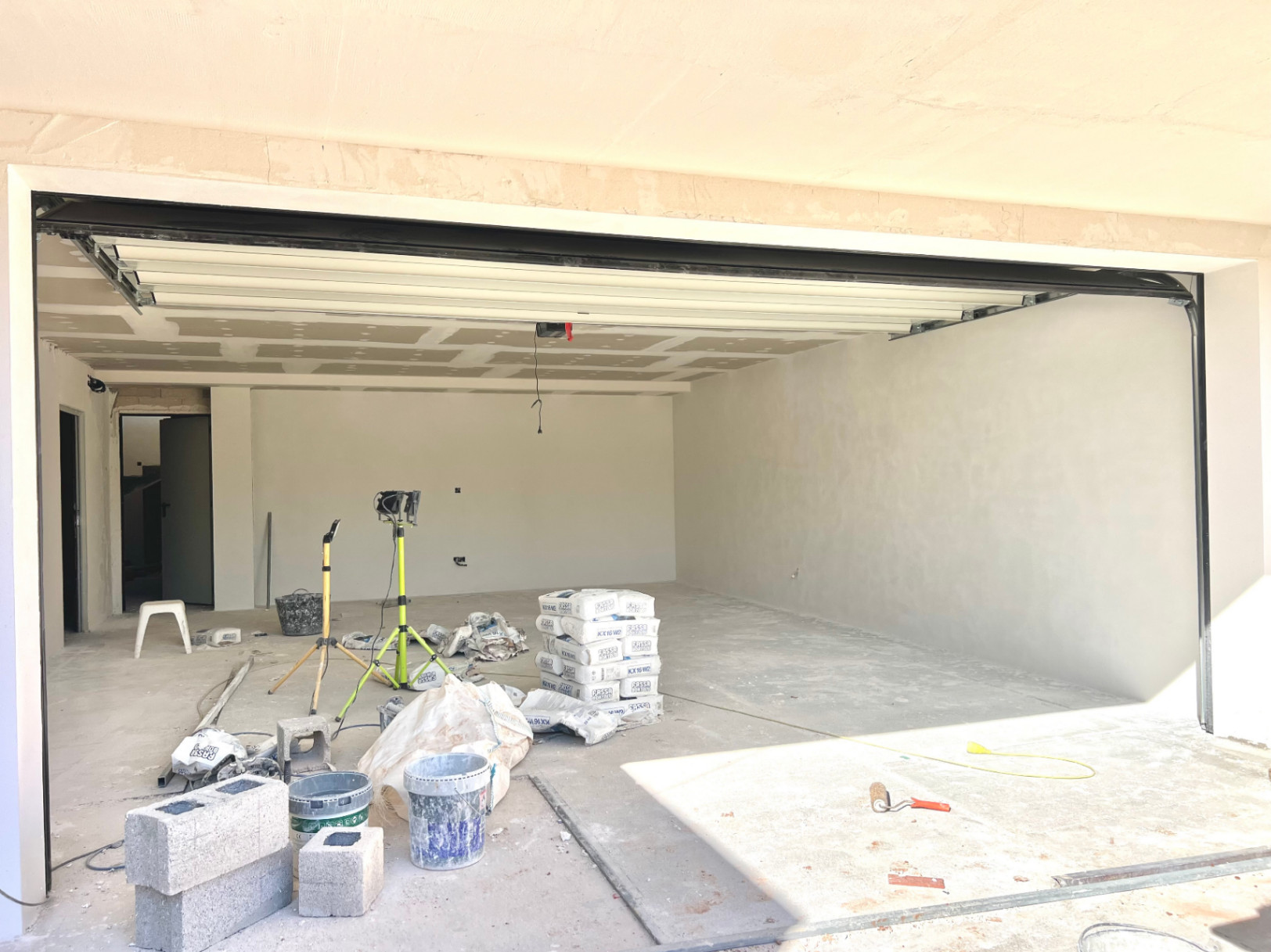 Geräumige Garage im Bau mit weißem Sektionaltor und hohen Decken, ideal für mehrere Fahrzeuge oder als zusätzlicher Hobbyraum.