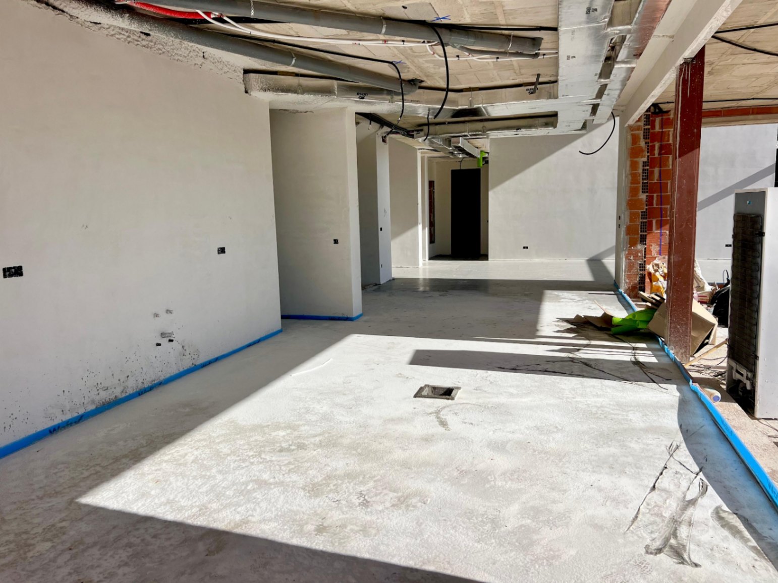 Innenansicht des Hauptgeschosses im Bau mit sichtbaren Deckeninstallationen, verputzten Wänden und Betonböden bei seitlichem Lichteinfall.