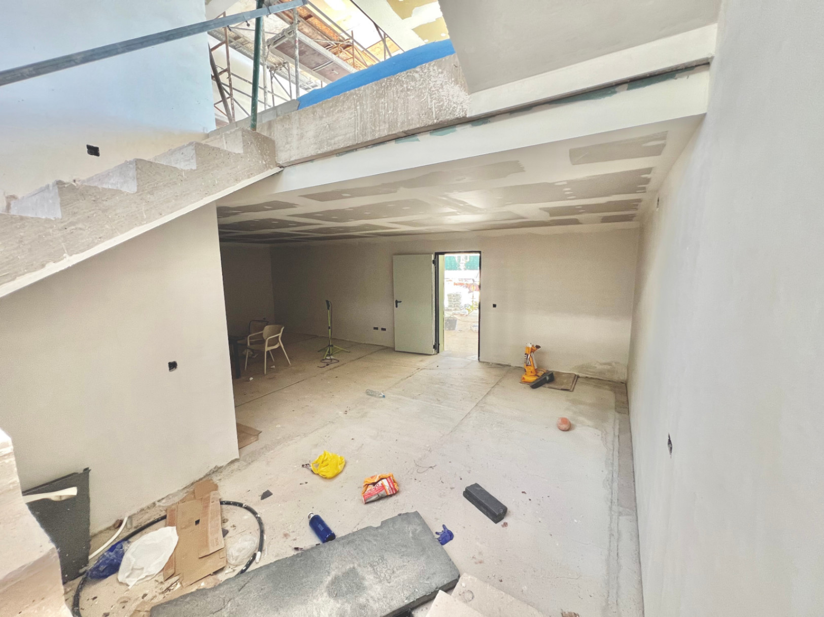 Innenansicht des Untergeschosses im Rohbau mit Betontreppe und großzügiger Mehrzweckfläche, ideal für einen Fitnessraum oder ein Heimkino.