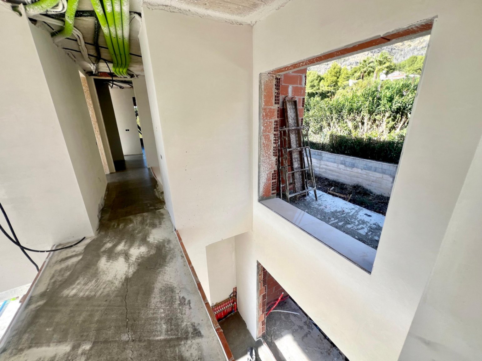 Innenflur in der Bauphase mit doppelter Deckenhöhe, sichtbaren technischen Installationen und einer großen Fensteröffnung zum Garten.