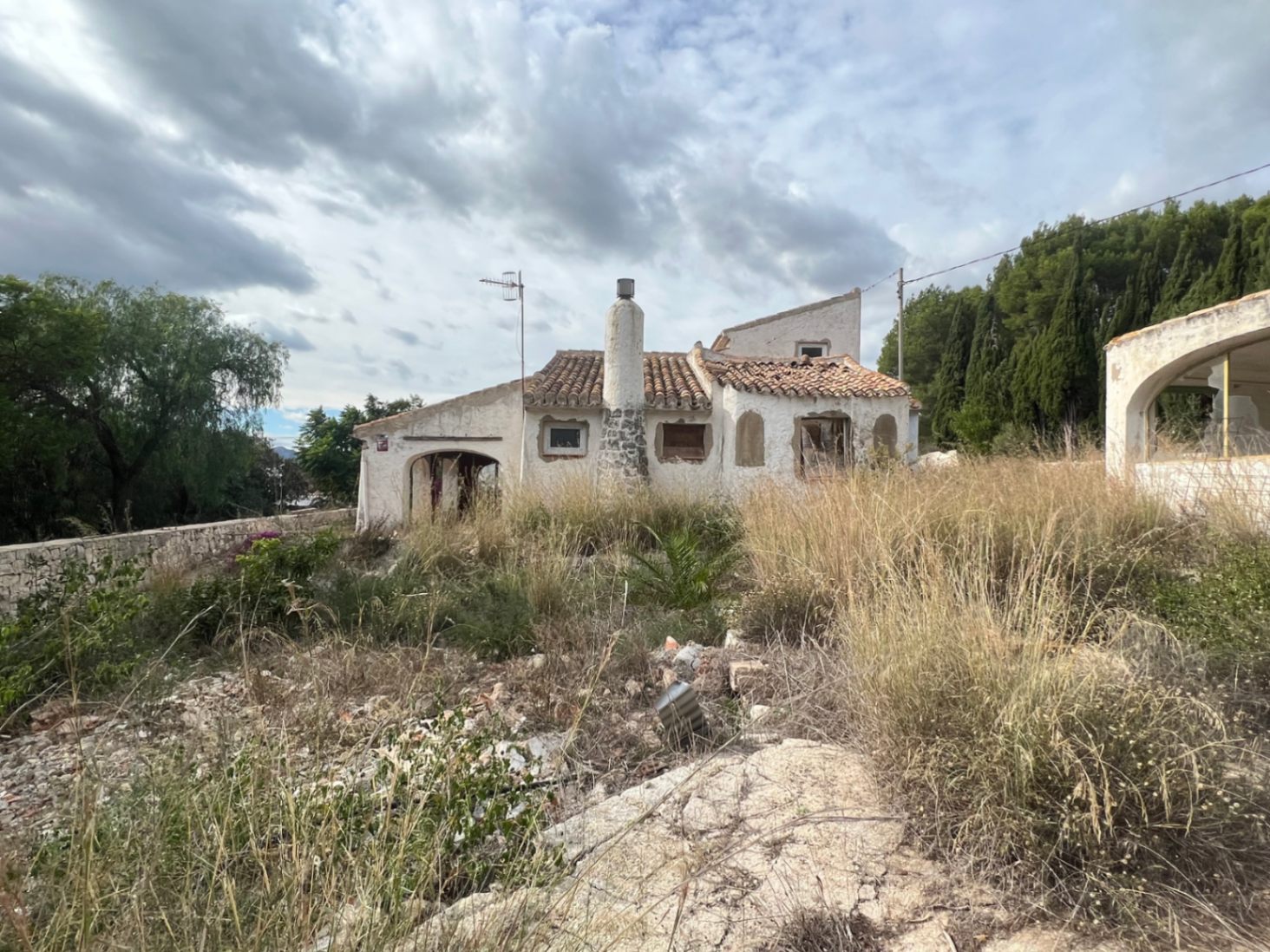Außenansicht der traditionellen Villa mit Steinkamin und Ziegeldach, gelegen auf einem großen Grundstück mit natürlicher Vegetation und Pinienbestand.