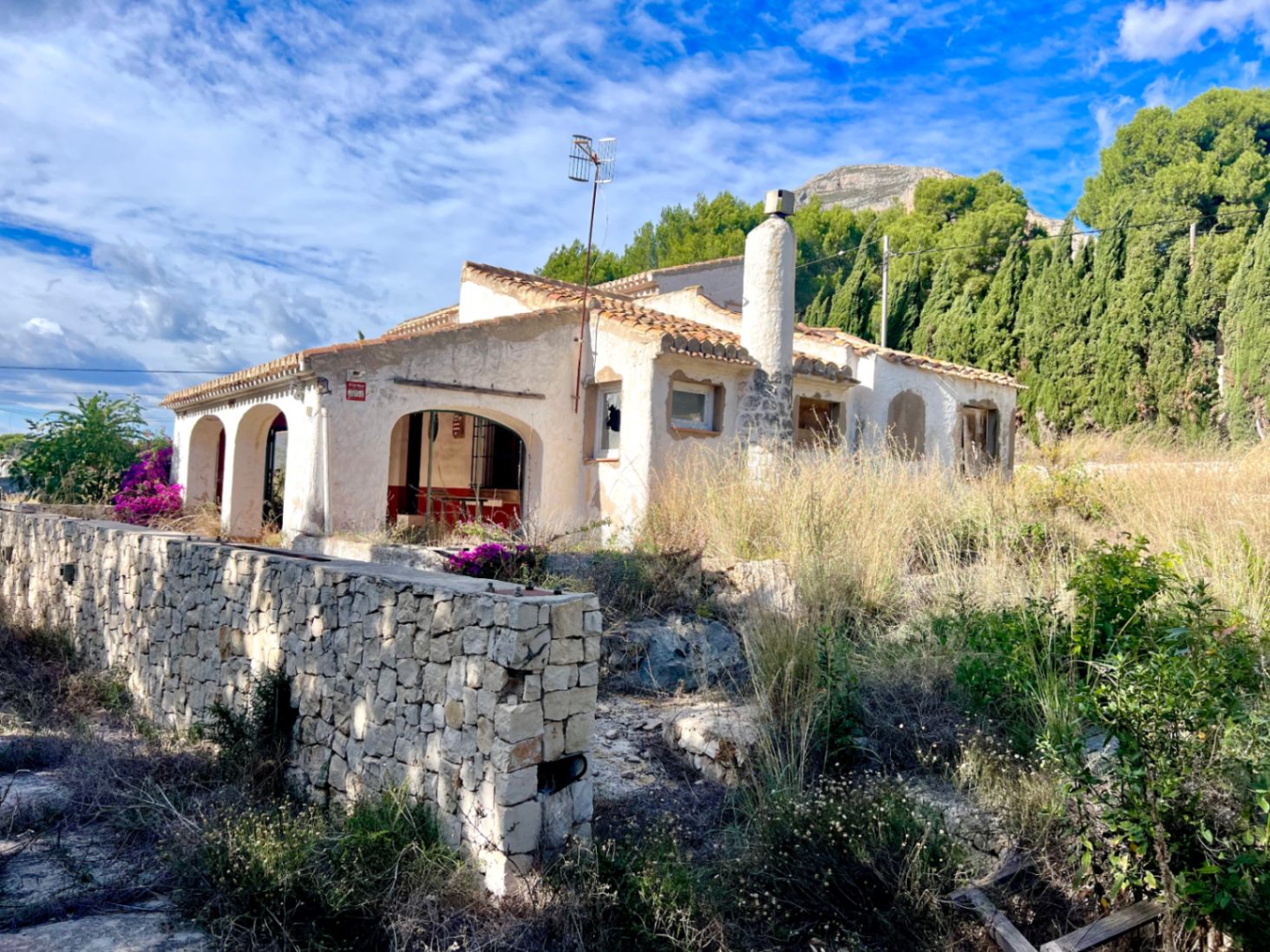 Außenansicht der Villa mit bogenförmiger Naya, Natursteinmauer und Ziegeldach vor der Kulisse des Montgó-Massivs in Jávea.