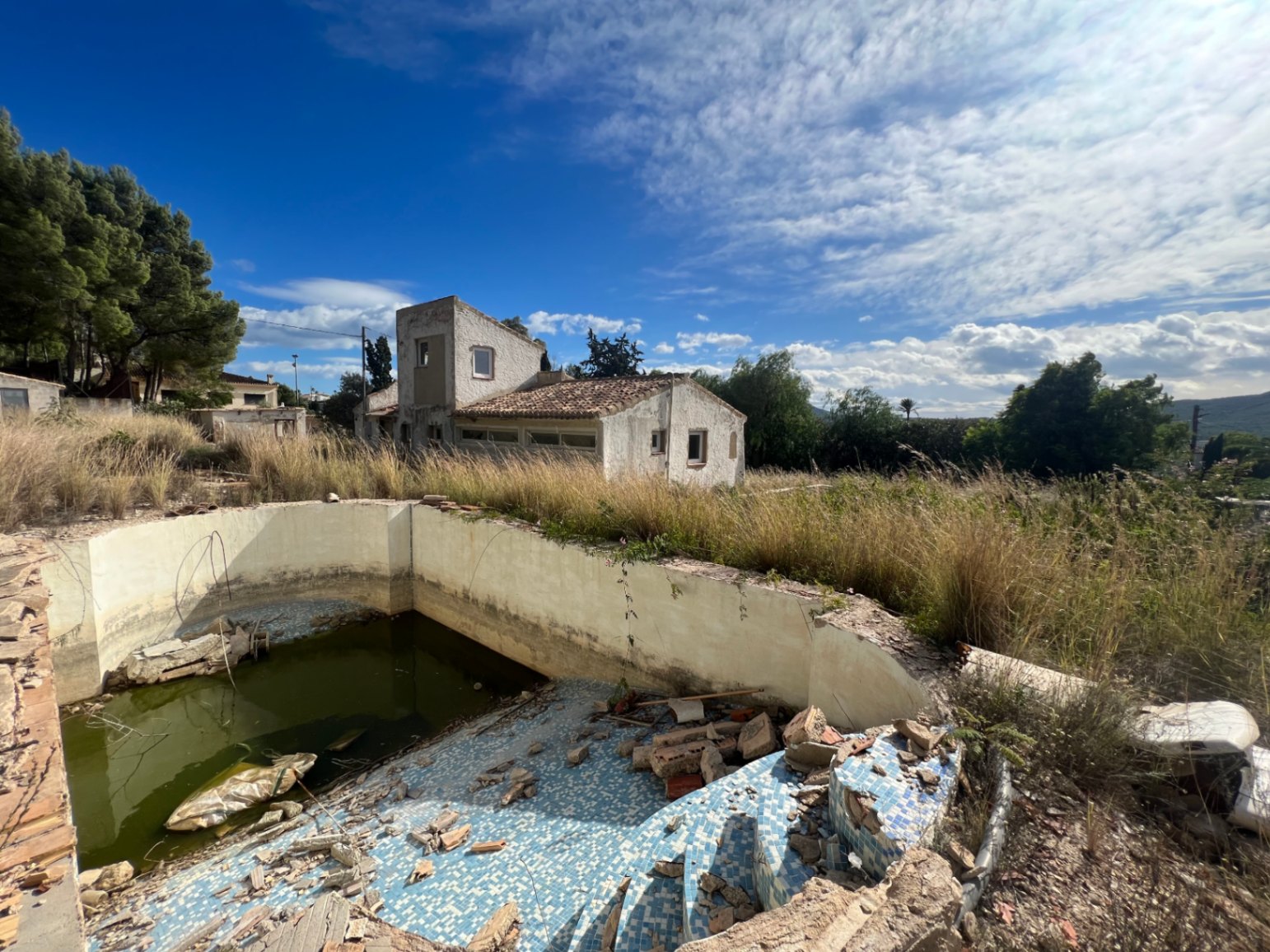 Außenansicht des Grundstücks mit renovierungsbedürftigem Pool und dem Haupthaus in sonniger Lage am Fuße des Montgó.