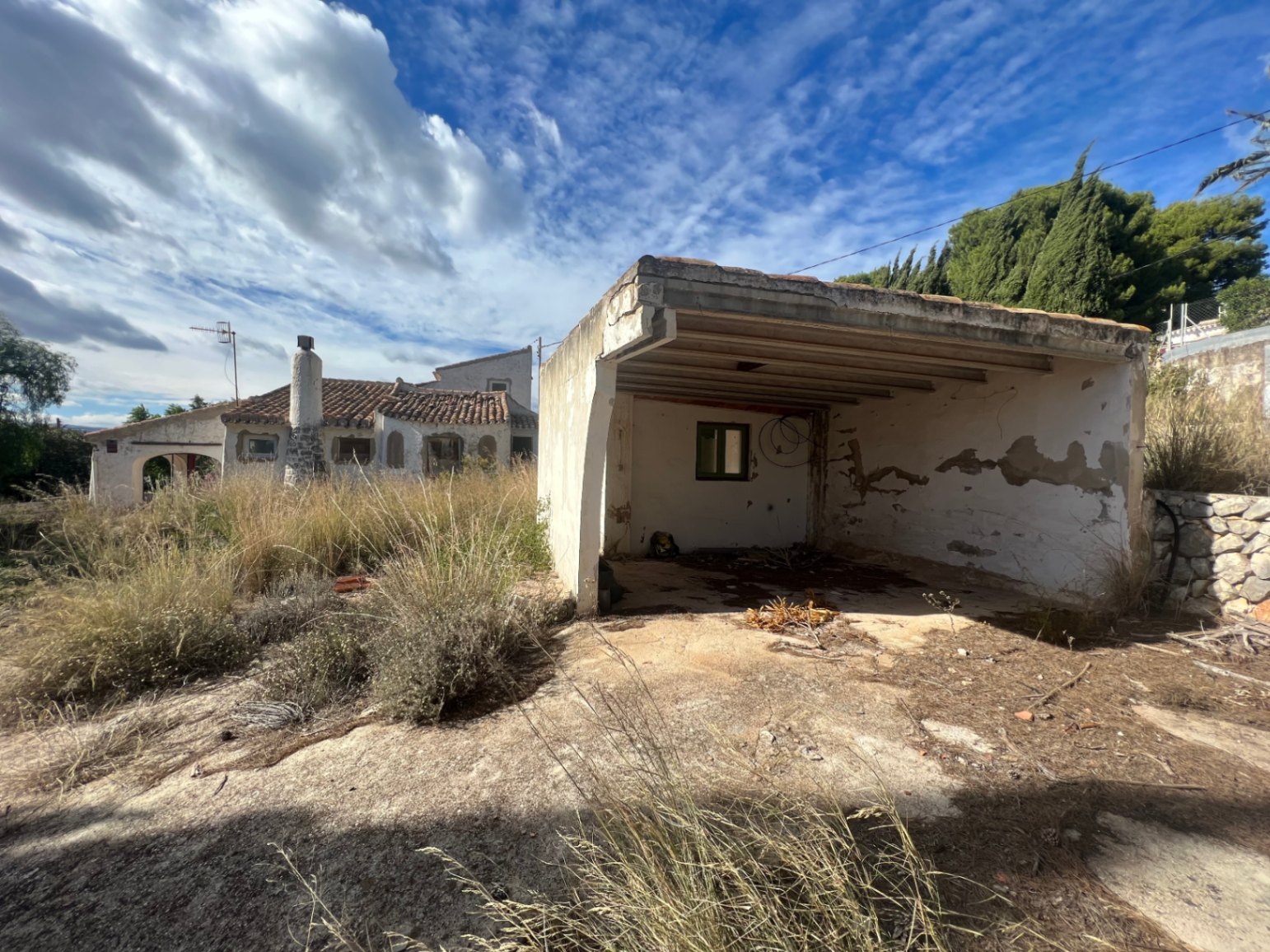 Freistehender Carport und Abstellraum in renovierungsbedürftigem Zustand auf einem großen Grundstück mit Blick auf das Haupthaus im mediterranen Stil.