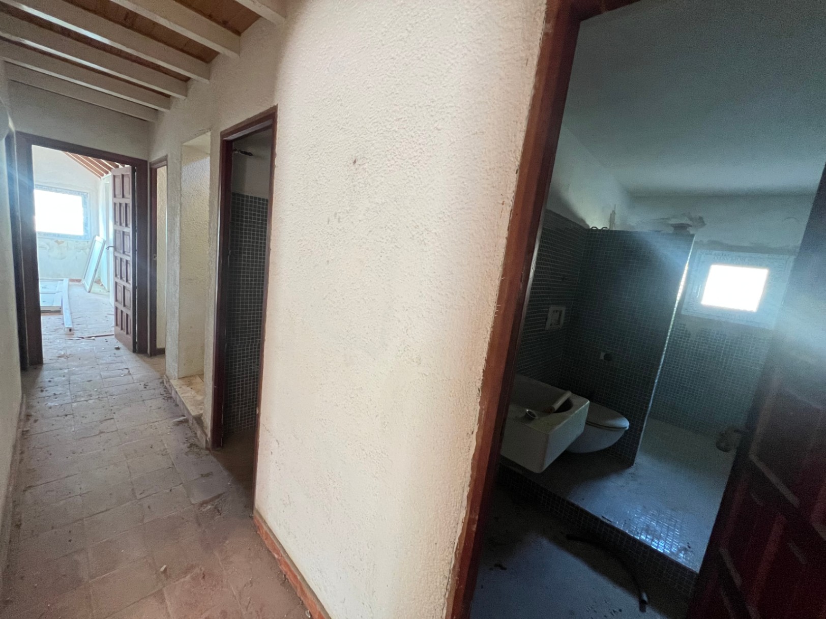 Innenflur mit sichtbaren Holzbalkendecken und Zugang zu einem Badezimmer mit blauen Mosaikfliesen. Der Raum verdeutlicht das umfassende Renovierungspotenzial.