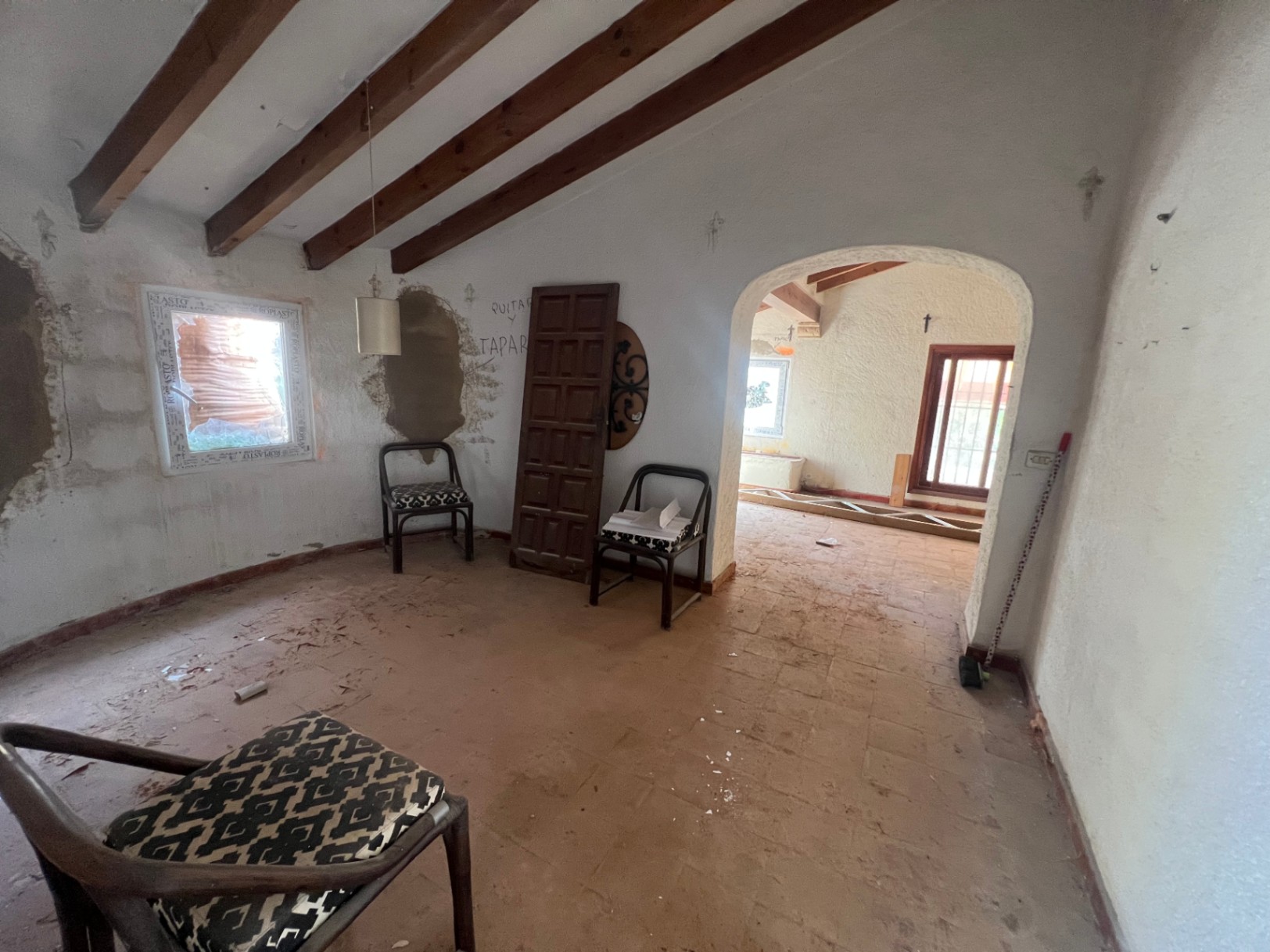 Innenraum mit sichtbaren Holzbalken an der Decke, Terrakottaboden und einem Rundbogen. Ein renovierungsbedürftiger Raum mit authentischen, rustikalen Bauelementen.