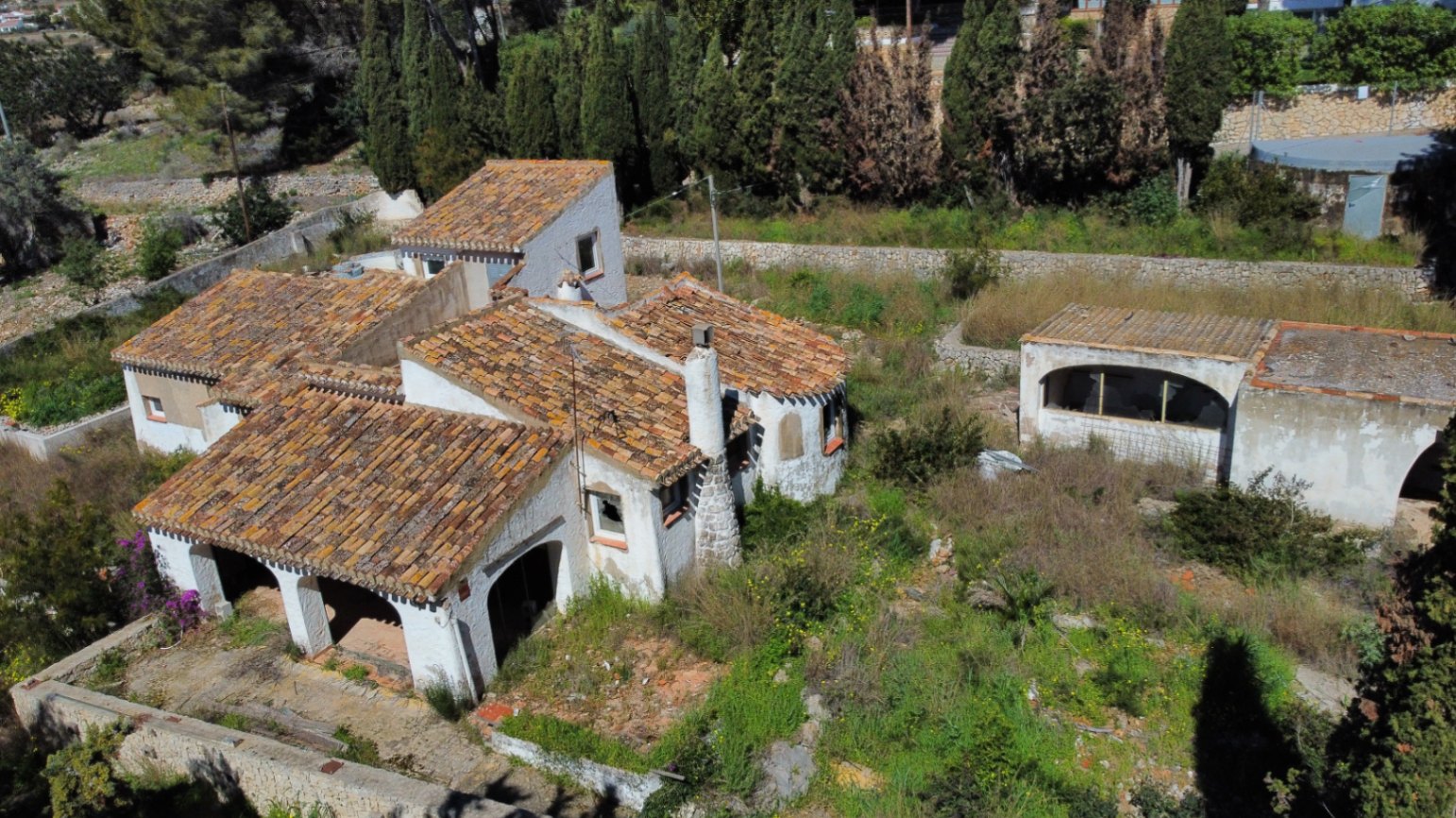 Luftaufnahme der Villa mit traditionellen Ziegeldächern, Rundbogenterrasse und Natursteinkamin auf einem weitläufigen, naturbelassenen Grundstück.