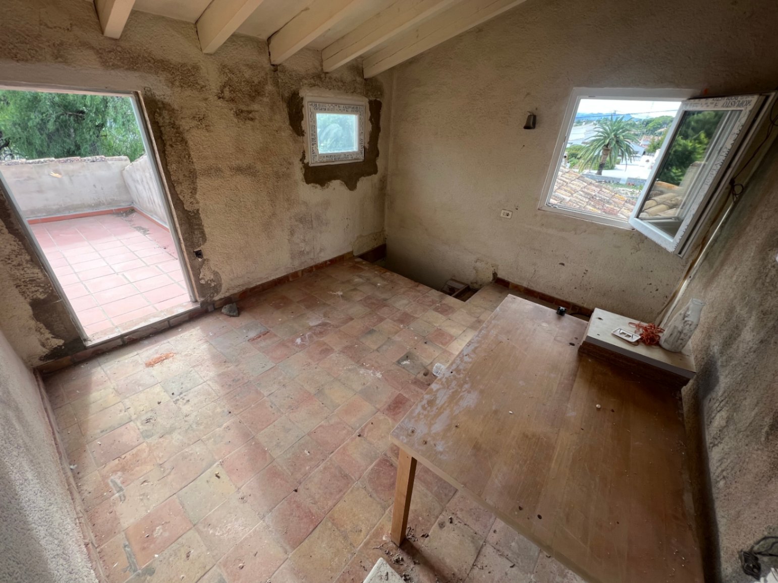 Obergeschoss-Zimmer mit sichtbaren Holzbalken, rustikalem Terrakottaboden und direktem Zugang zu einer privaten Terrasse mit weitem Ausblick.