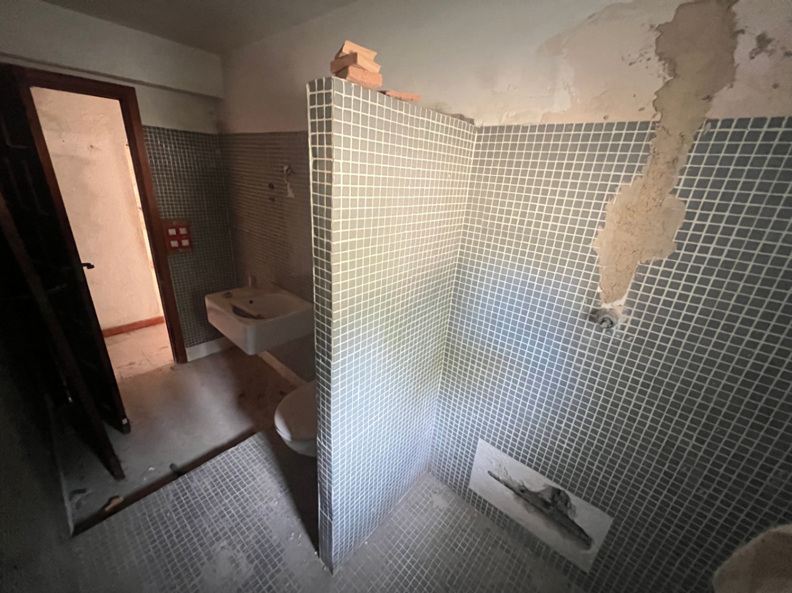 Originales Badezimmer mit blauen Mosaikfliesen, Trennwand und Sanitärobjekten. Der Raum erfordert eine umfassende Renovierung zur Modernisierung der Ausstattung.