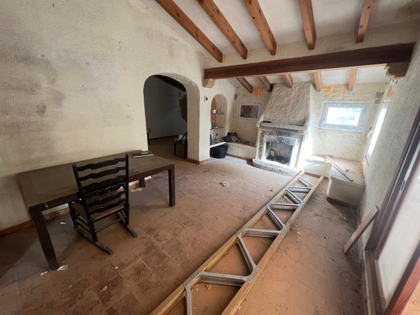 Rustikales Wohnzimmer zum Renovieren mit sichtbaren Holzbalken, traditionellem Kamin und Terrakottaboden. Rundbögen führen in die angrenzenden Räume.