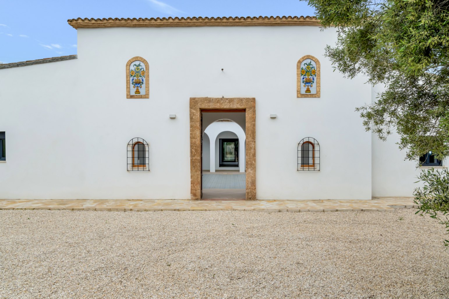 Mediterrane weiße Fassade mit einem Eingang aus Tosca-Naturstein, dekorativen Keramikfliesen und Blick in den bogenförmigen Innenhof.