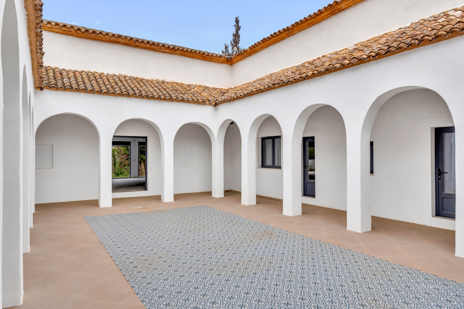 Mediterraner Innenhof mit weißen Rundbögen, Terrakottaboden und einem zentralen Bereich aus gemusterten Fliesen unter traditionellen Ziegeldächern.