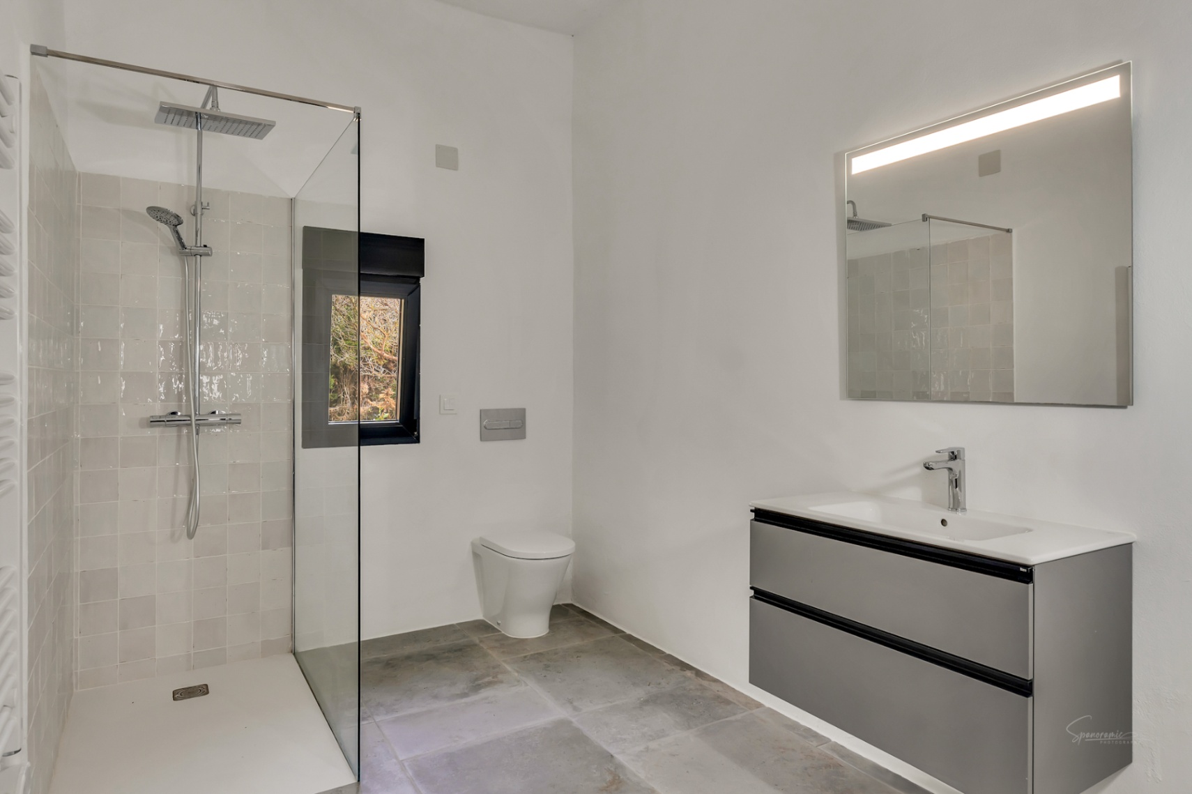 Modernes Badezimmer mit begehbarer Dusche, Glastrennwand, wandhängendem WC und schwebendem grauem Waschtisch mit beleuchtetem Spiegel.