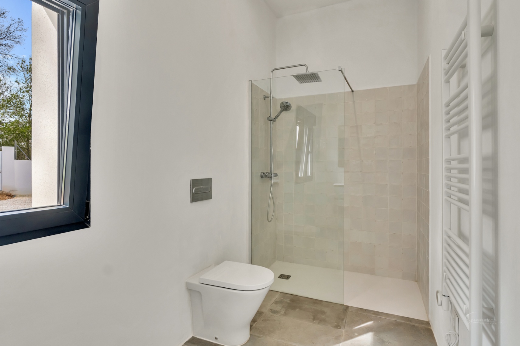 Modernes Badezimmer mit bodengleicher Dusche, Glastrennwand und beigen Fliesen. Es bietet ein wandhängendes WC, einen Handtuchheizkörper und Natursteinböden.