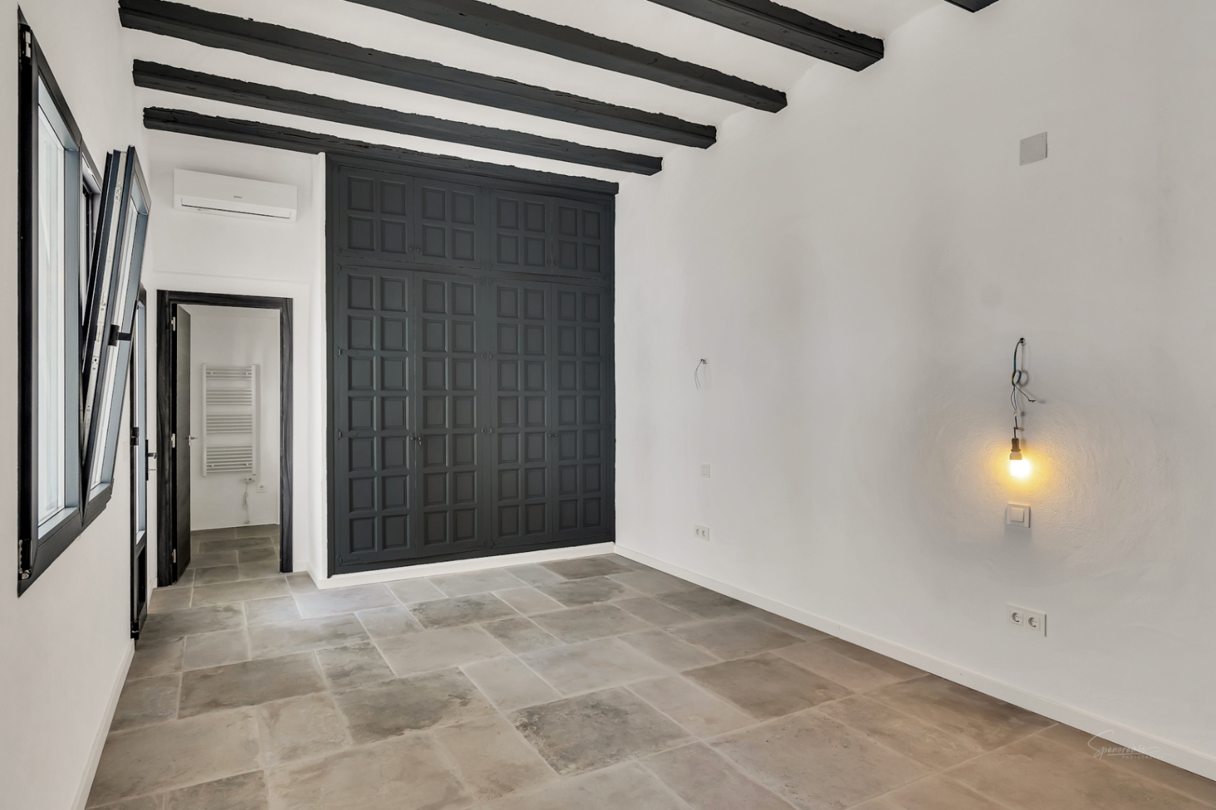 Schlafzimmer mit dunklen Sichtbalken, Natursteinboden und einem großen, anthrazitfarbenen Einbauschrank mit traditioneller Kassettenoptik.