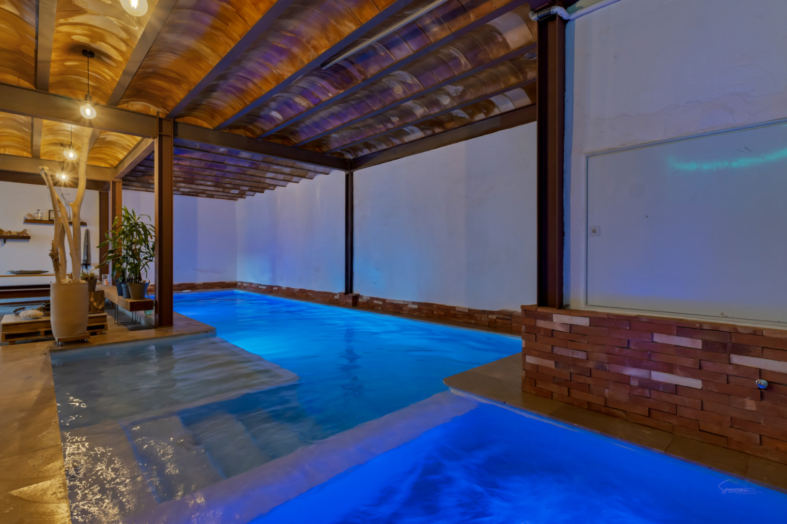 Beheizter Innenpool mit blauer LED-Beleuchtung, gewölbten Terrakotta-Decken und freiliegenden Stahlträgern in einer rustikal-industriellen Optik.