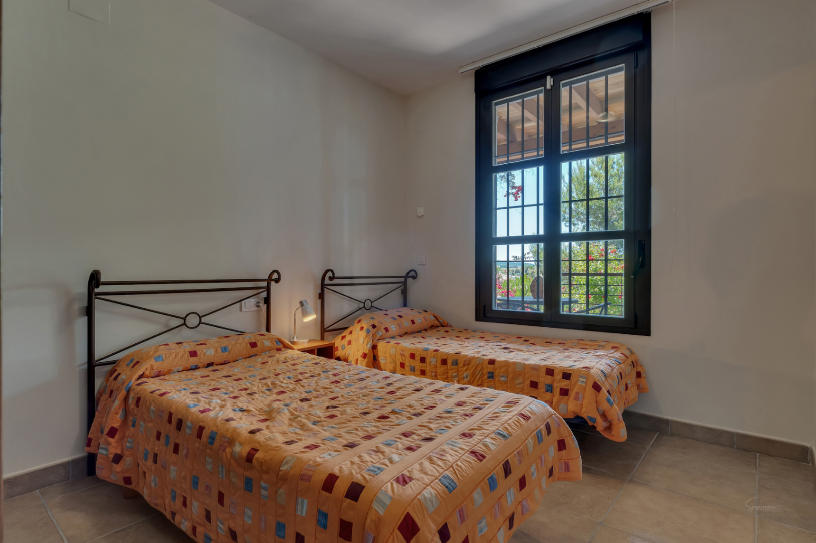 Helles Schlafzimmer mit zwei Einzelbetten, schmiedeeisernen Kopfteilen und Fenster mit Blick auf den gepflegten Garten.