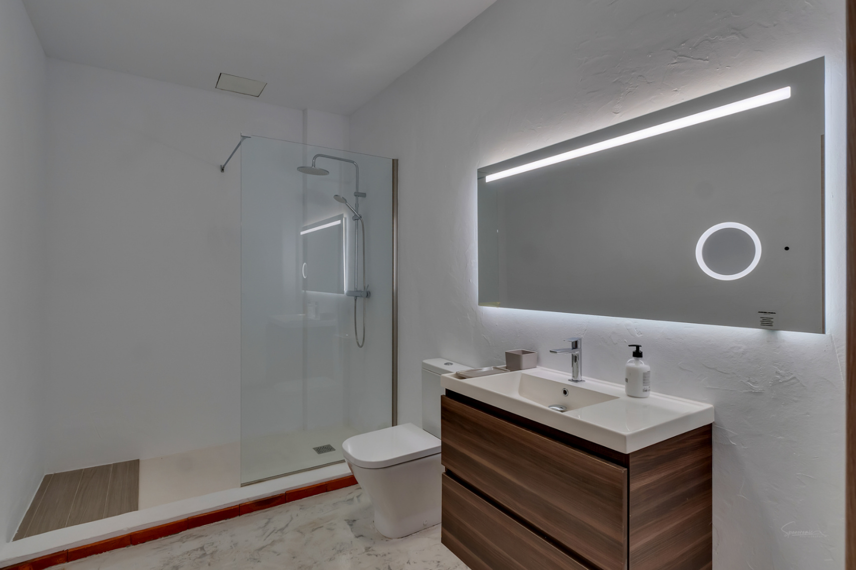 Modernes Badezimmer mit schwebendem Waschtisch in Holzoptik und großem LED-Spiegel. Es bietet eine begehbare Dusche mit Glastrennwand und weiße Wände mit Strukturputz.